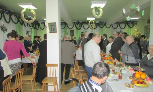 Zdjęcie przedstawia dużą liczbę uczestników. Duża część z nich stoi przy stole, reszta zaś siedzi.