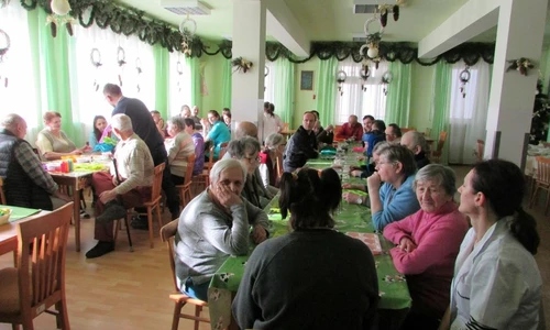 Zdjęcie przedstawia dużą ilość osób siedzących przy stolikach w jednym pomieszczeniu.