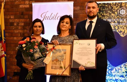 zdjęcie grupowe trzy osoby trzymają okolicznościowe gratulacje i kwiaty